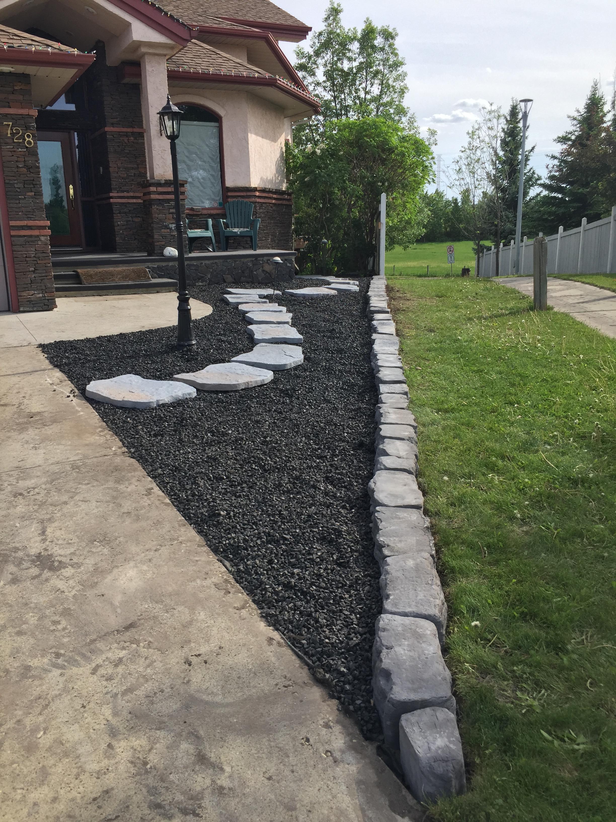 Front yard black gravel bed with stepping stones and stone block edging